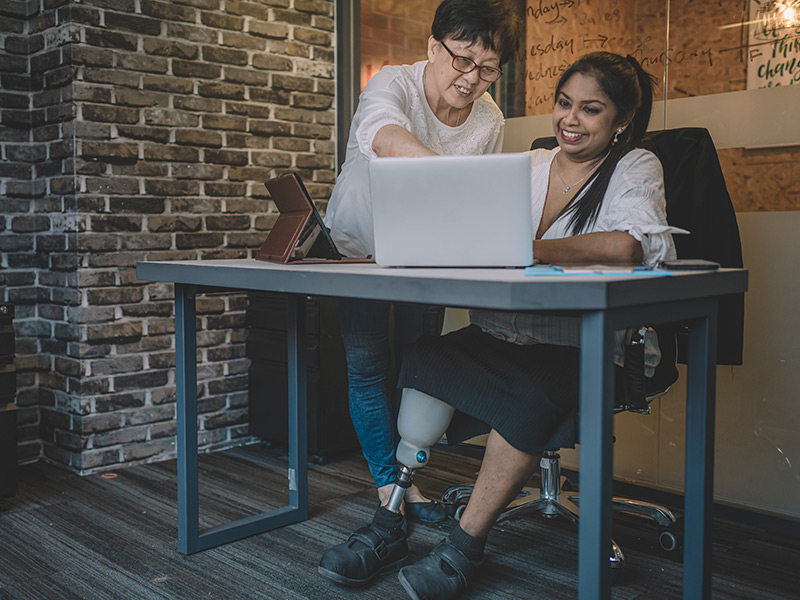Image of woman with a prosthetic leg working in an office with a colleague.