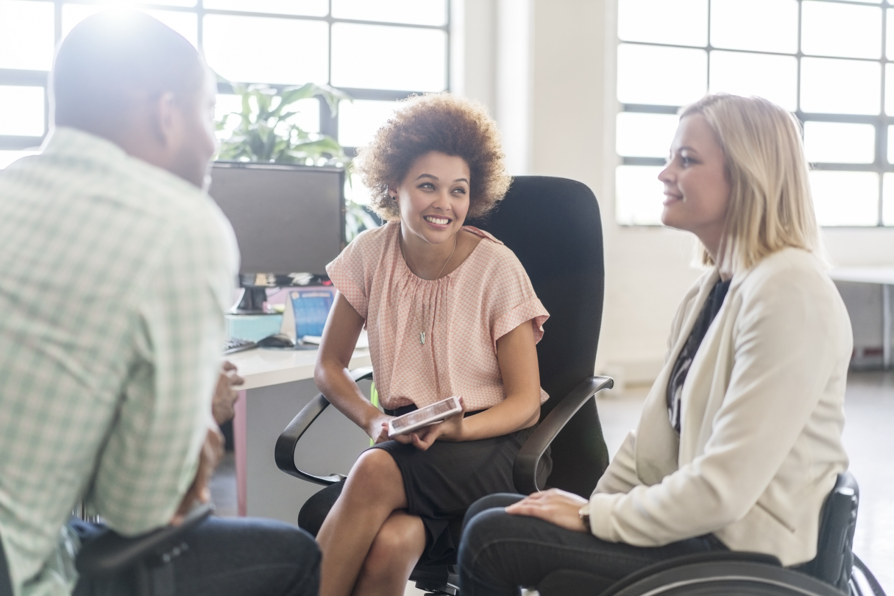 Image of diverse group of individuals conversing a workplace, including one woman who uses a wheelchair.